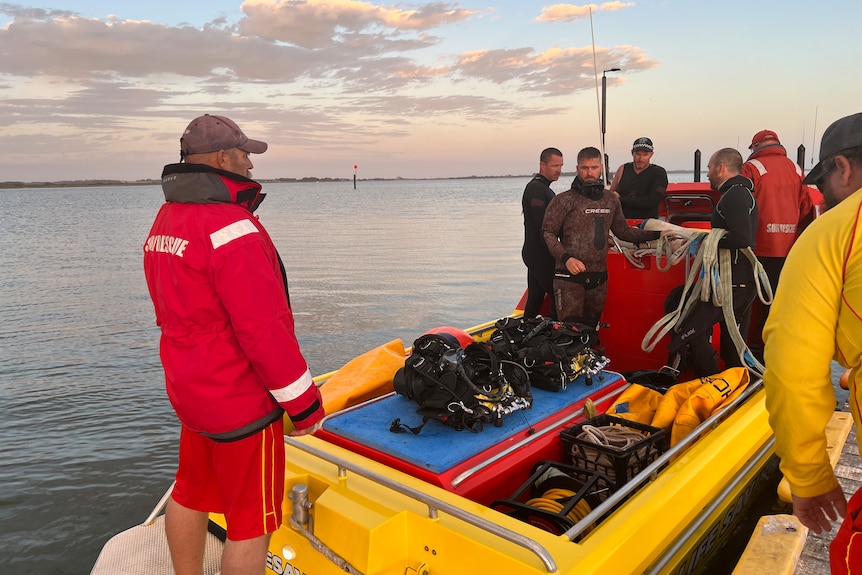 A group of people stand on a boat near a boat ramp holding roeps and other equipment