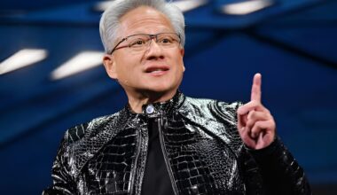 A person wearing a shiny black jacket is gesturing with their finger against a blurred blue background.