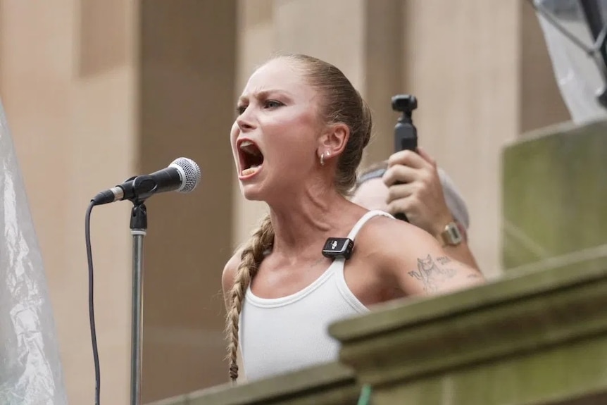 Grace Tame speaks into microphone on balcony.