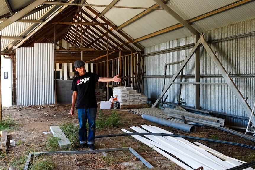 A man standing in a tin shed, pointing.