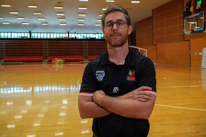 Chris Earl stands next to a basketball with his arms folded. 