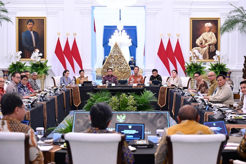 A rectangular table surrounded by a number of people, men and women, in the palace.