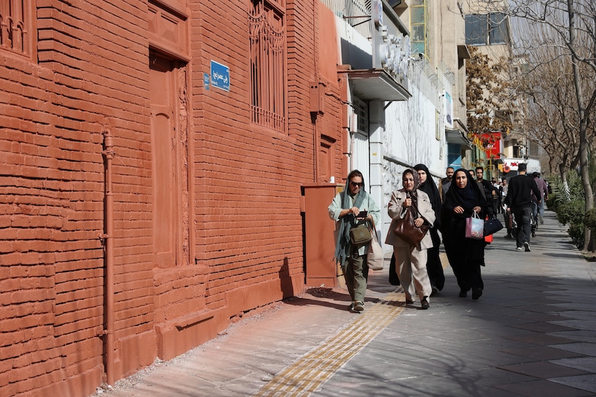 Women wearing hijabs rush along a street in Tehran, Iran.