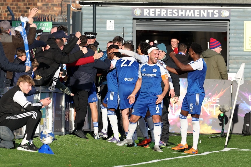 Serveral footballers celebrating with a large crowd of people.