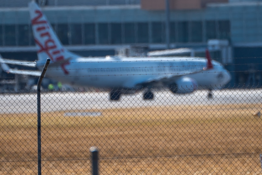 A Virgin plane seen from far away with an airport building behind