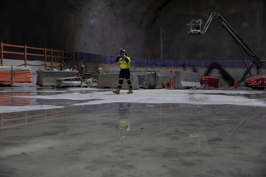 A construction worker walking along concrete underground. 