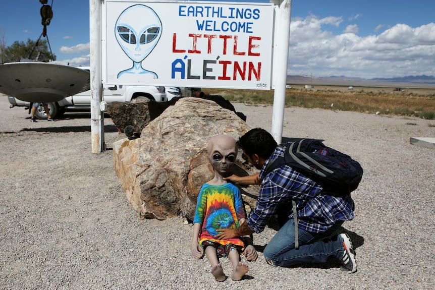 A man holding a fake alien outside an US establishment called Little Ale Inn.