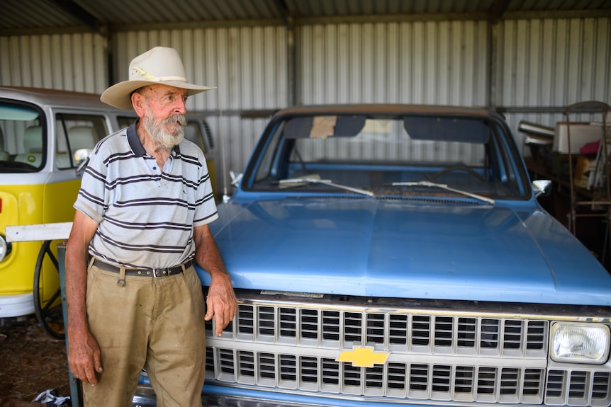 Mervyn is walking in-front of an old blue Chevy truck. There is also a bright yellow VW Kombi in the background. 