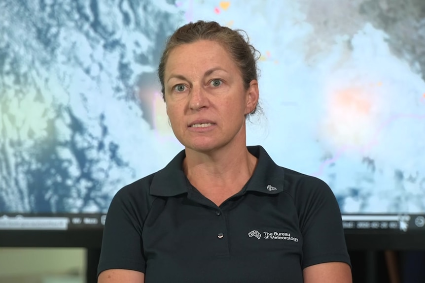 Caroline wears a black BOM polo shirt and is pictured in front of a satellite image