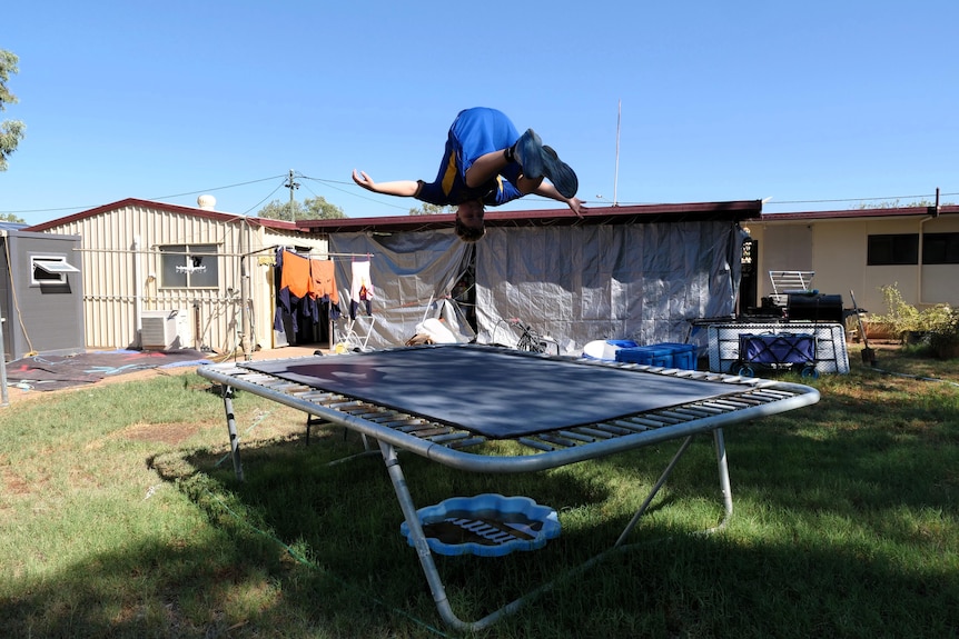 Boy in school uniform doing flip on trampoline in backyard.