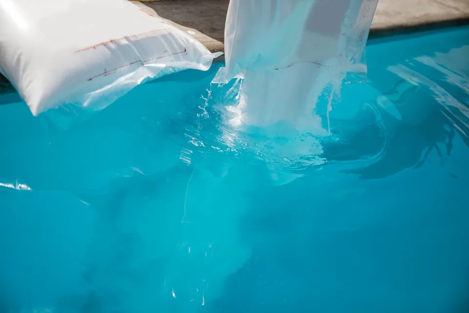 Water being poured into a swimming pool from a large bag, creating ripples on the surface