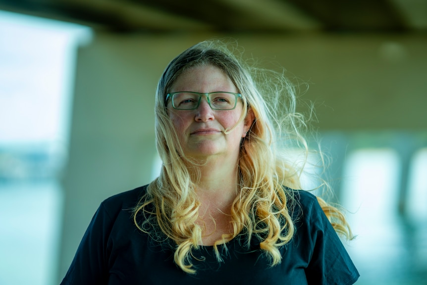 A woman looks into the camera, her hair blows in the wind.