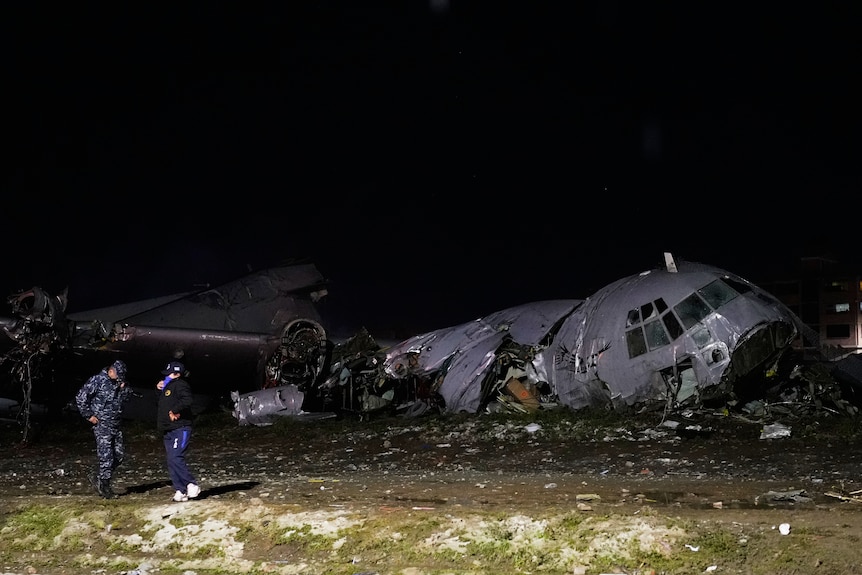 Uniformed police stand next to a crumpled crashed plane.