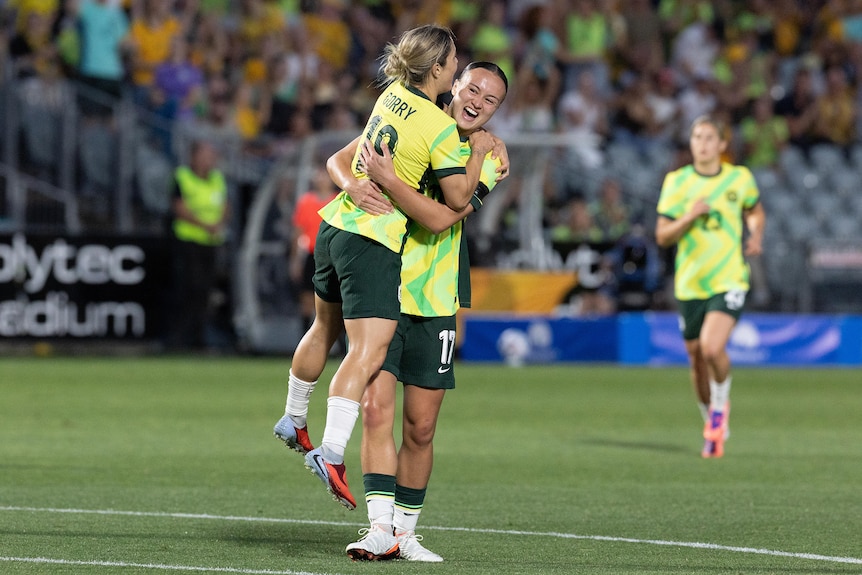 A Matildas player jumps into the arms of a teammate who has just scored in an international.