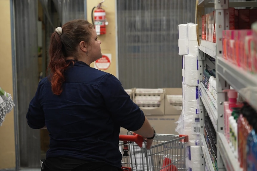 A young woman pushes a trolley down a supermarket aisle.