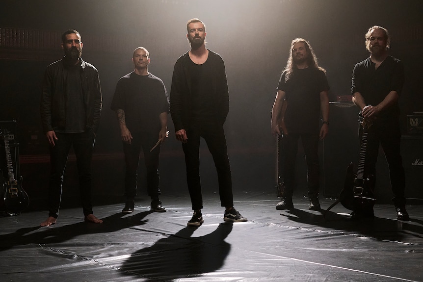 Five members of Aussie band Karnivool pose on stage under glowing light