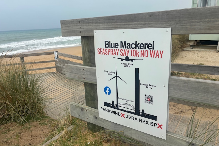 A protest sign saying "Blue Mackerel Seaspray say 10k no way" with a picture of wind turbines is posted up near a beach.