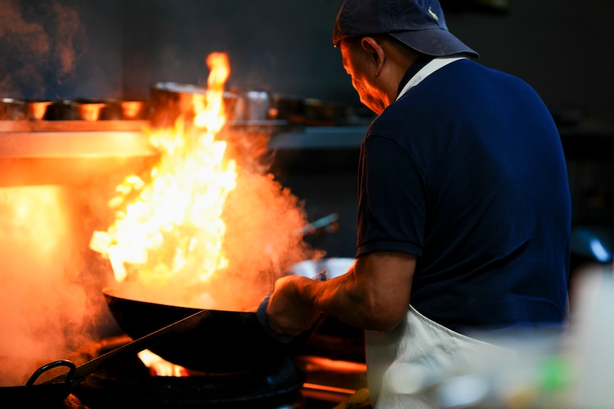 A man firing up a wok inside a kitchen.