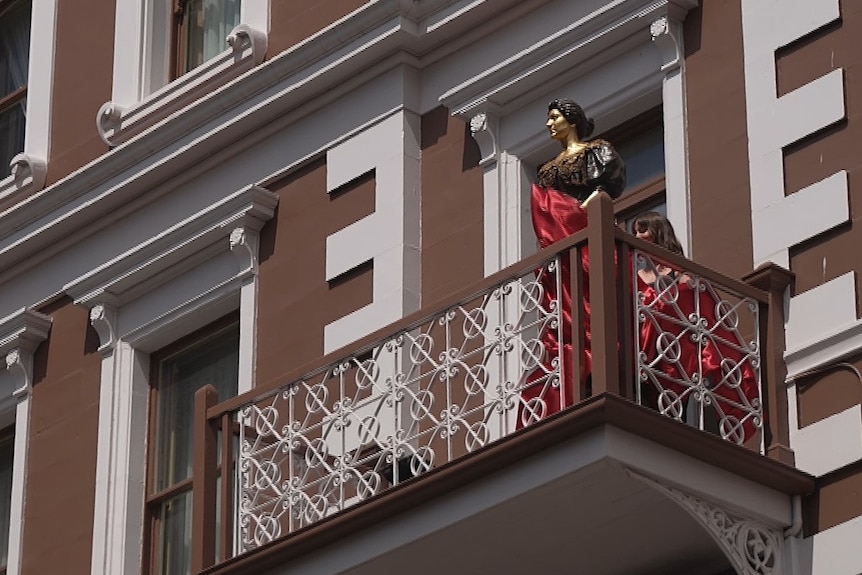 Bronze statue of a woman on the balcony of a building.