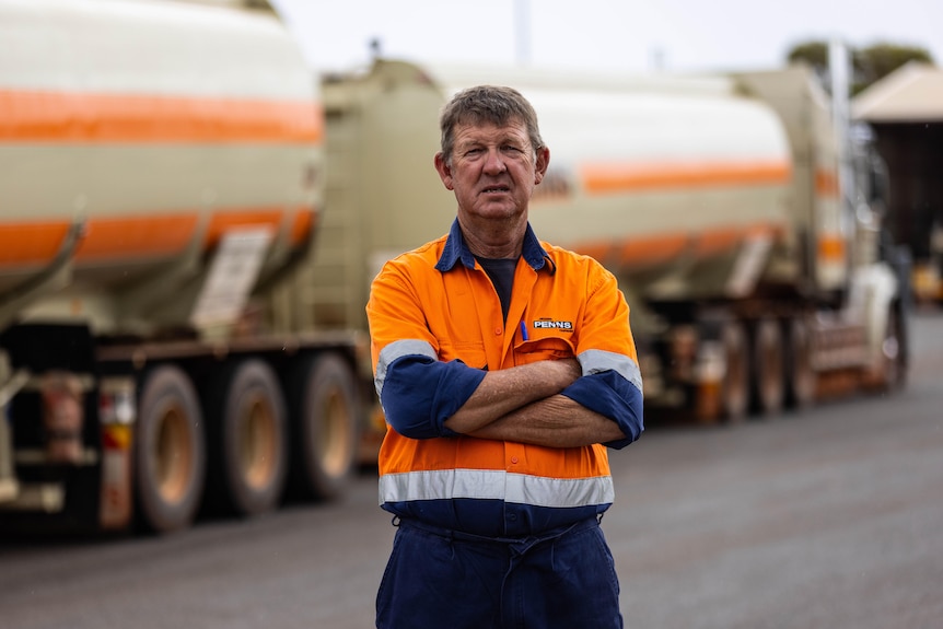A man in high-vis workwear standing in front of a road train.  