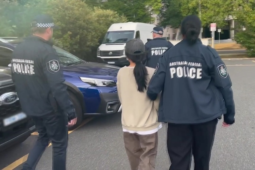 A woman is escorted across a street by three uniformed officers.