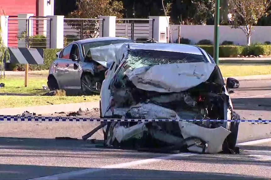 Two wrecked cars in a sunny suburban street with police tape stretched across the road. 