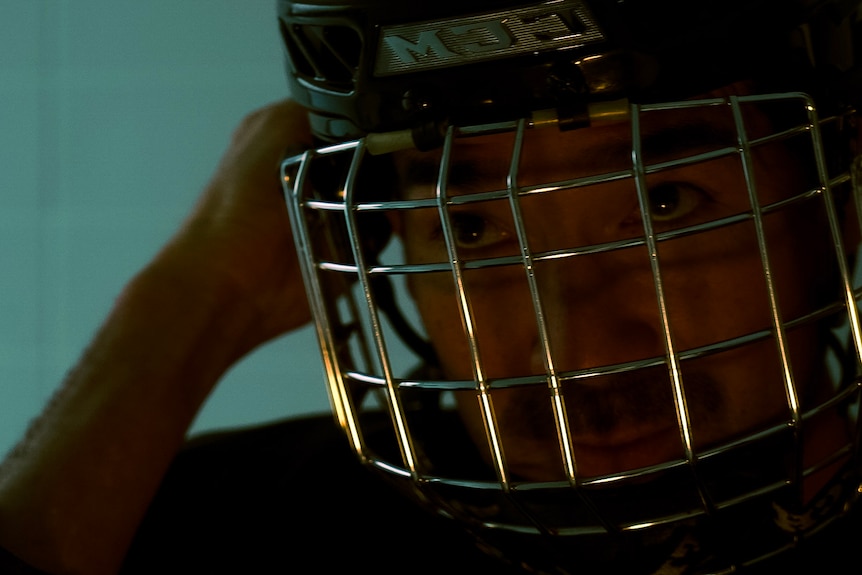 Man putting on ice hockey helmet.