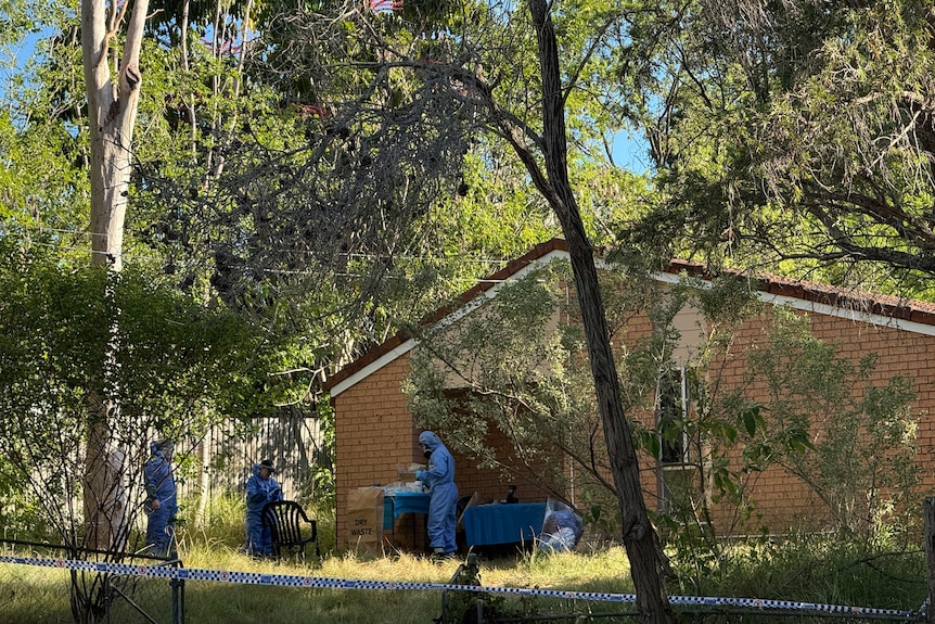 People in scrubs at a house behind police tape.