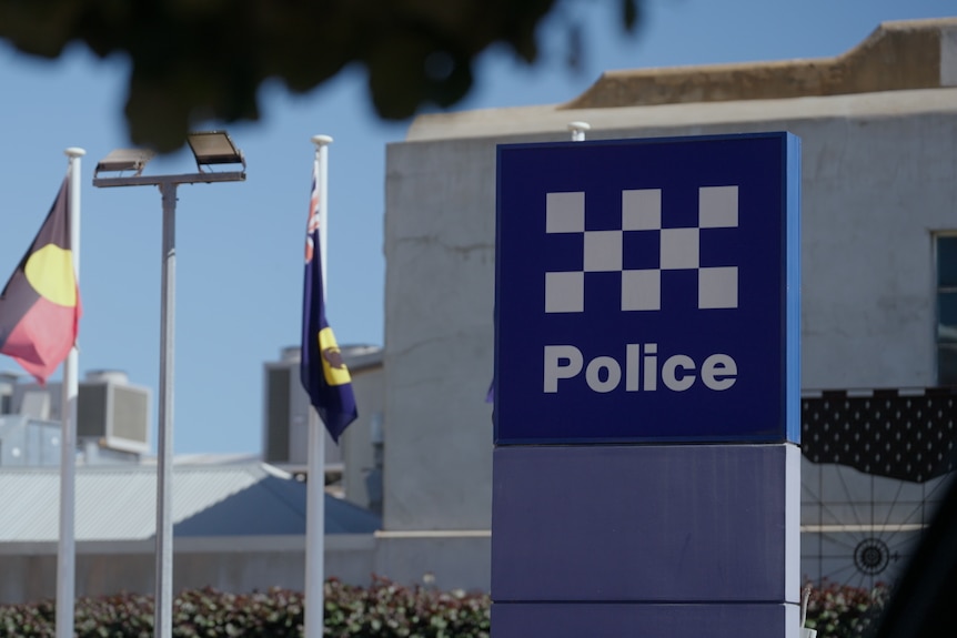A blue and white police station sign with an Aboriginal and Australian flag behind it