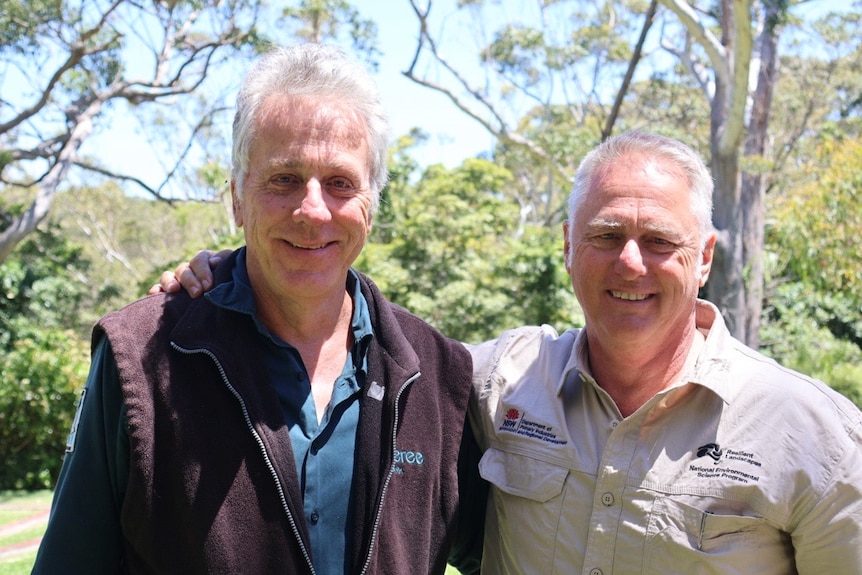 two men smiling trees behind them