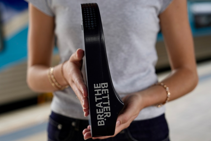 Ms Rollo holding a skinny black invention that looks like a chair without legs with the phrase 'breathe better' on it.
