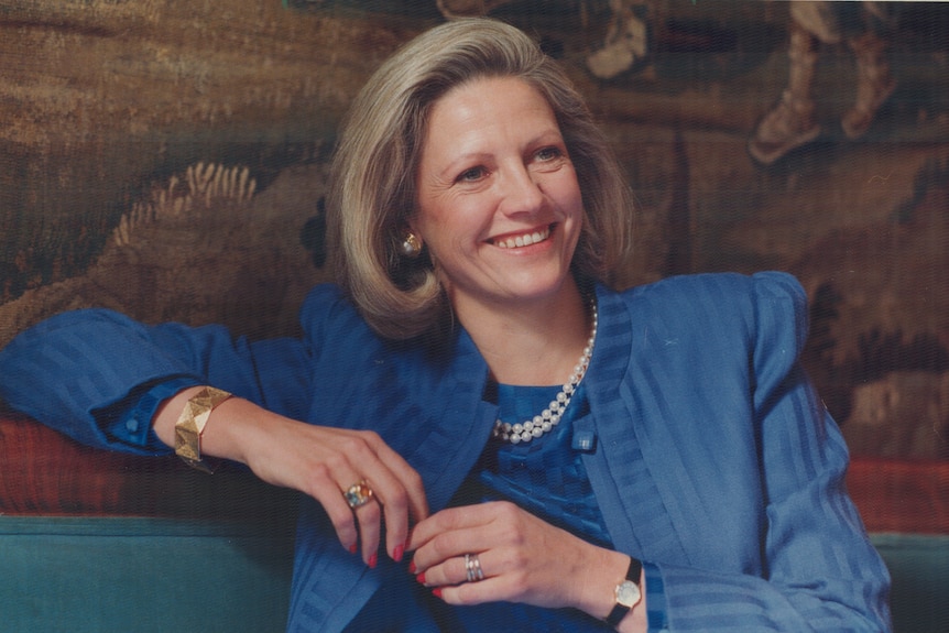 A woman with short blonde hair and a blue blazer, smiles at the camera