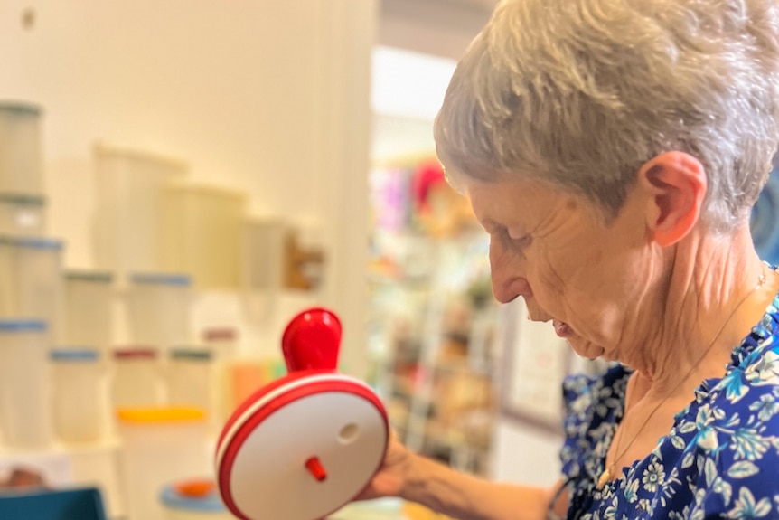 A lady in blue looks at red tupperware in a shop front