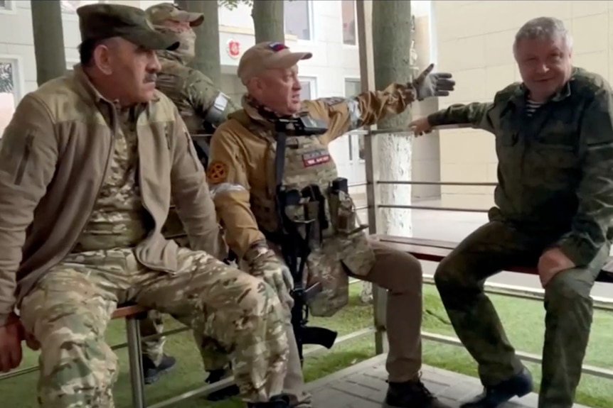 Four men in military fatigues chat.