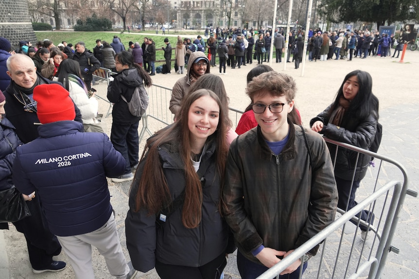 Two young people smile for a photo while standing at the head of a long line