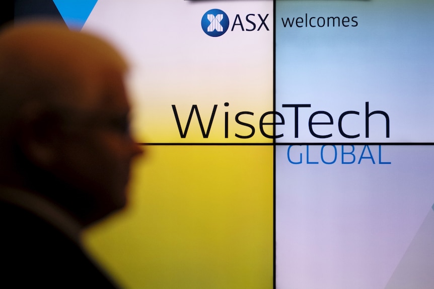 The blurred side profile of a man walking past a screen that says "ASX welcomes WiseTech Global".