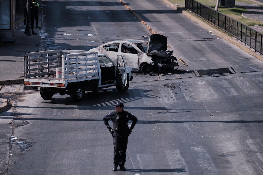 A police officer stands in front of two burned cars.