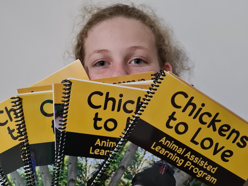 A young child peeks out from behind a stack of books.