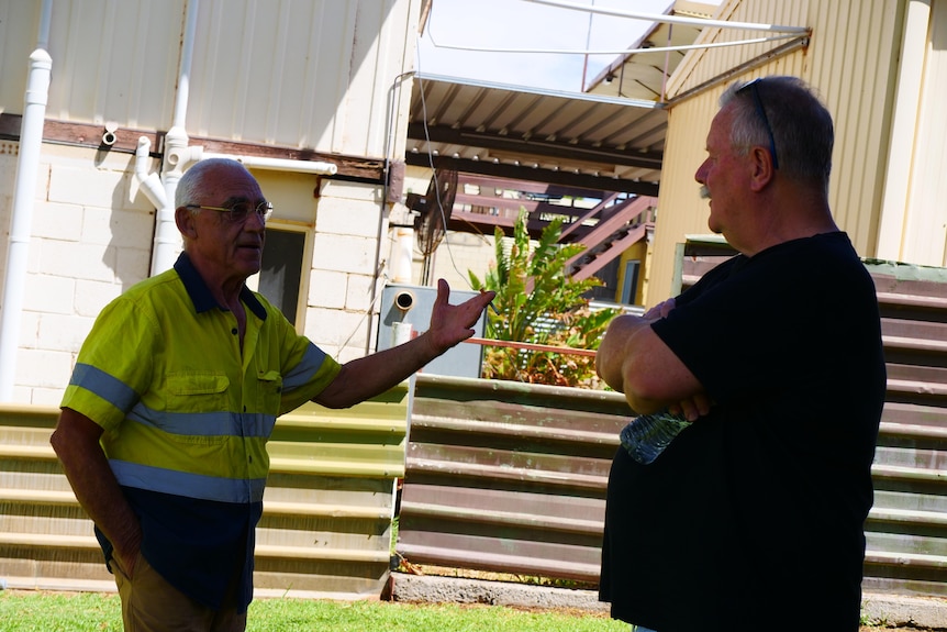 Two men face each other talking in a backyard