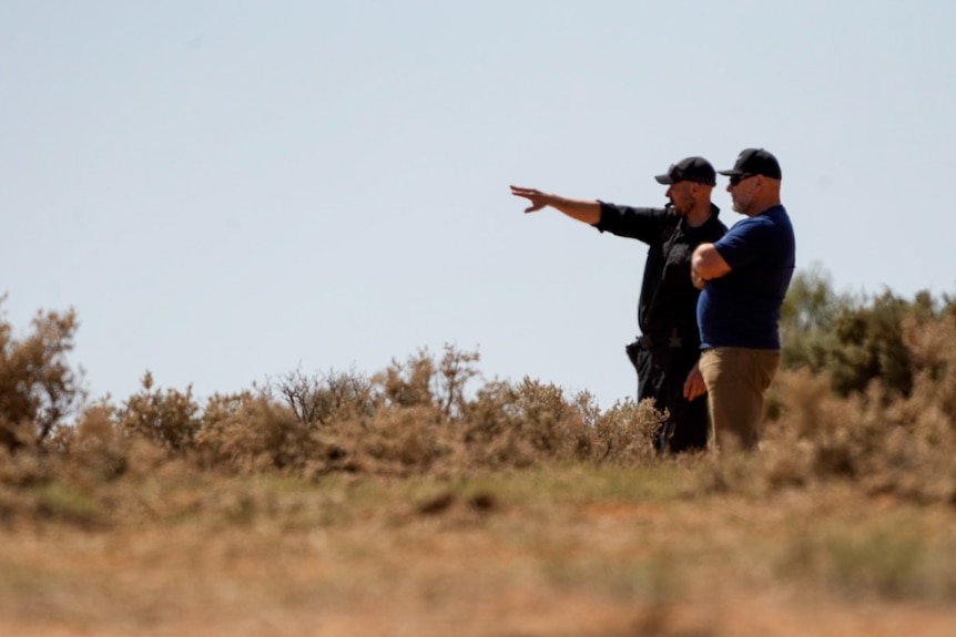 A police off points off into the distance, while standing next to another man 