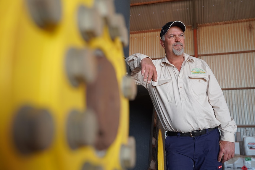 A man in agricultural attire leans on the side of a tractor.