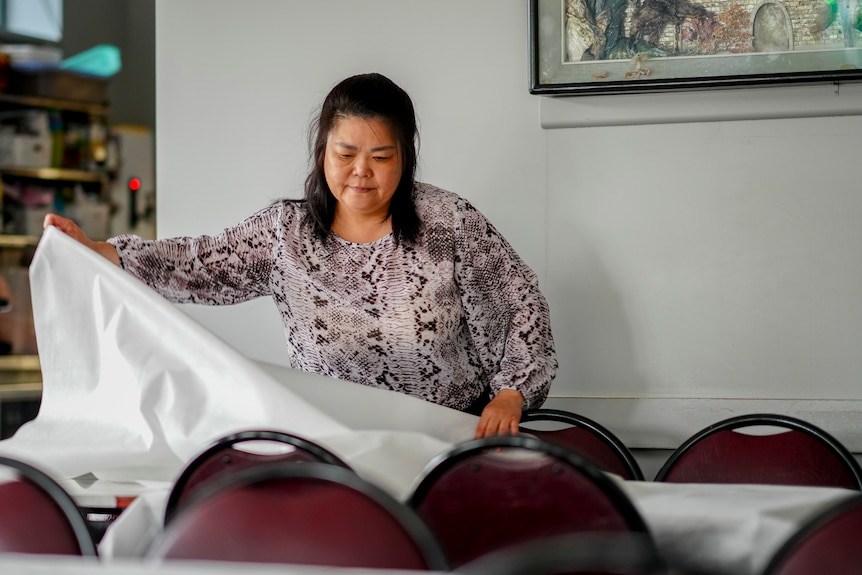 A woman waving a white cloth and placing them on top of a rectangular table.
