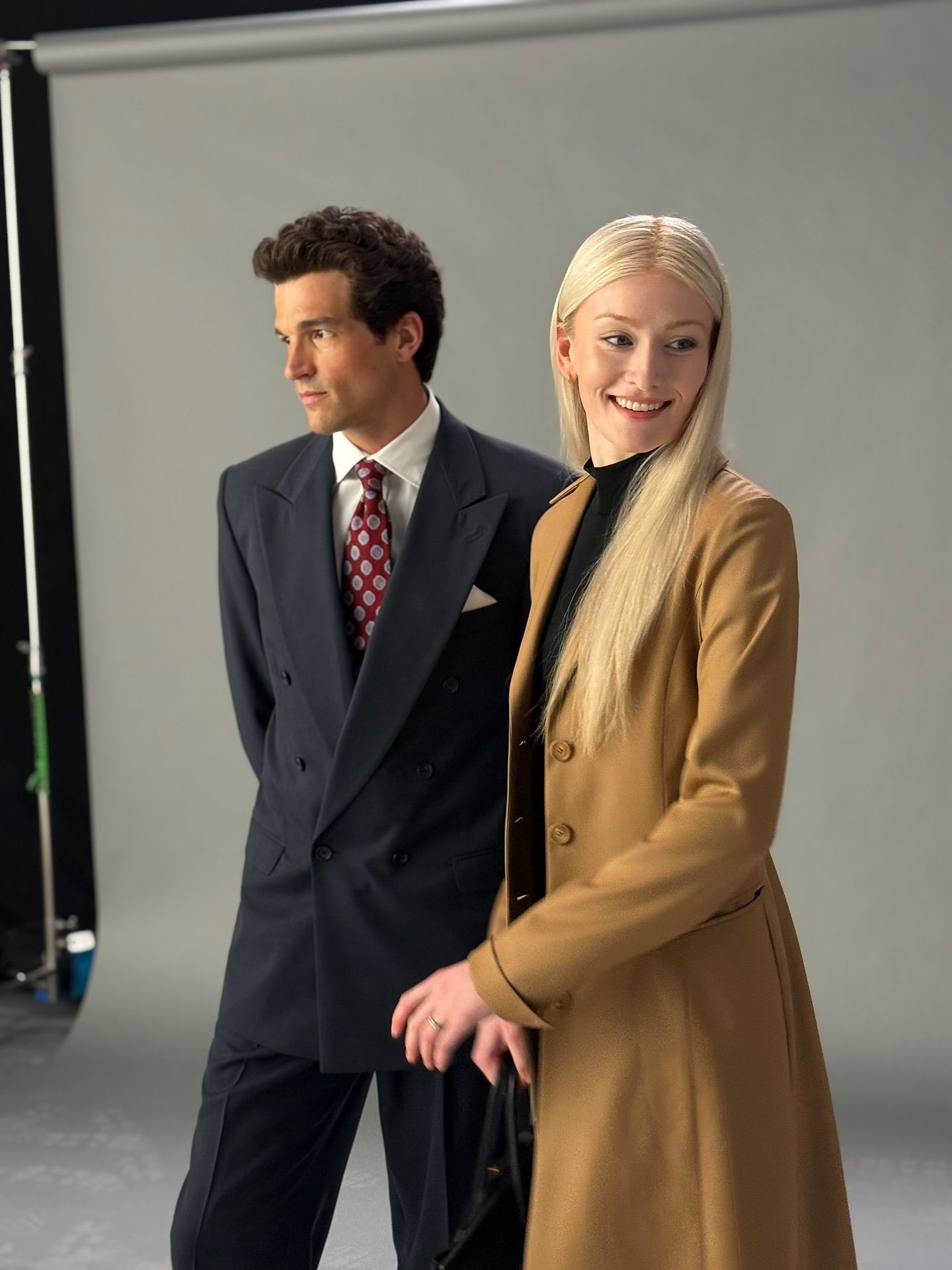 A dark-haired man and a blonde woman pose in front of a screen.