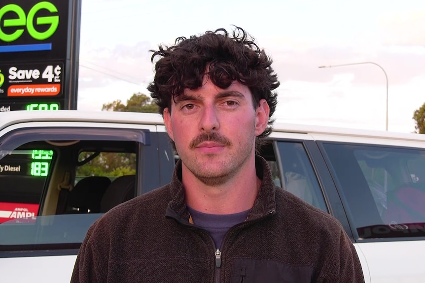 Man stands and looks at camera in front of car. 