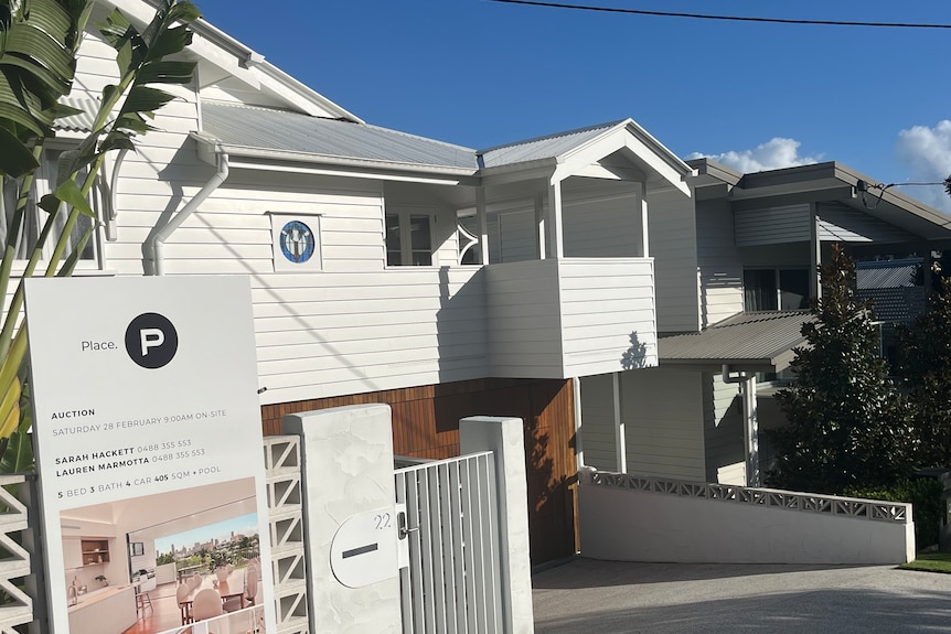 A street in the Brisbane suburb of Norman Park with a for sale sign outside a white house. 