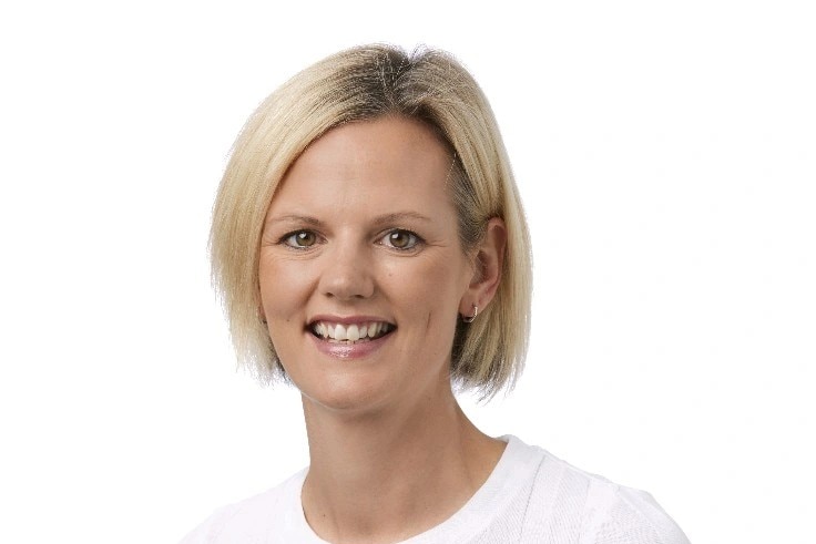 A woman in a white shirt and blonde bob smiles at camera.