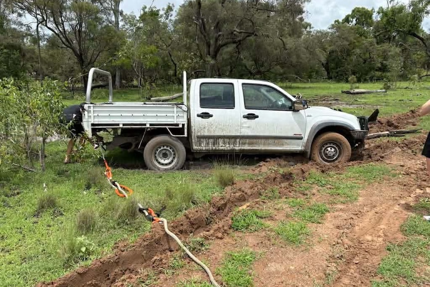 A white ute bogged on the side of a road.