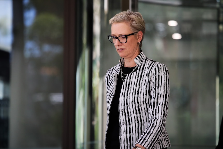 Kirsten Nelson, wearing a black and white striped top, leaves court looking down.