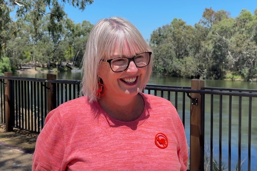 A woman in a pink top smiles in front of a river