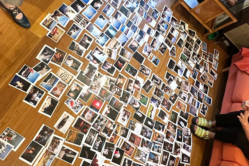 Dozens of photos lie in rows on a wooden lounge room floor.